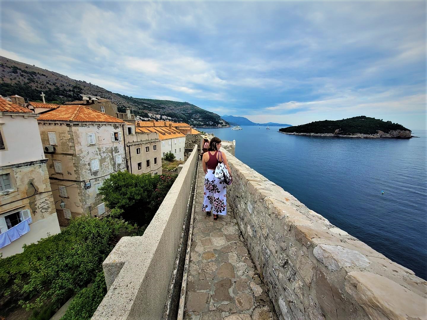 A girl walking along the city walls of Dubrovnik looking out over the ocean.